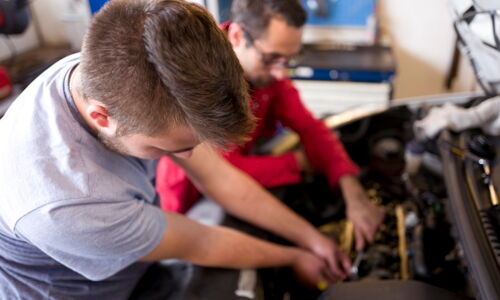 Ein Jugendlicher und ein Mann arbeiten im Motorraum eines Autos