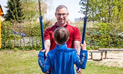 Ein Mann hält eine Schaukel, auf der ein Kind sitzt