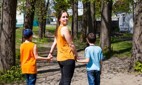 Eine junge Frau geht mir Kindern an der Hand spazieren und dreht sich dabei um