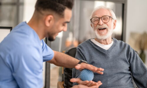 Ein junger Physiotherapeut massiert die Hand von einem älteren Mann mit einem Massageball