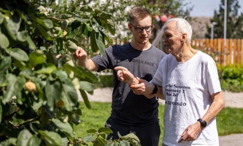 Ein junger Mann und ein älterer Herr sind im Garten bei einem Obstbaum.