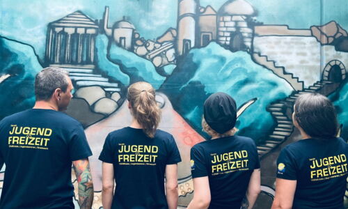 Man sieht Betreuer:innen von hinten mit einem Shirt, auf dem Jugend und Freizeit steht.