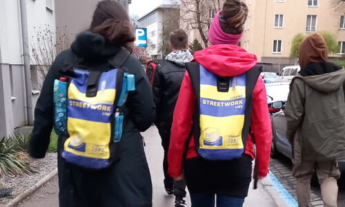 Man sieht Frauen von hinten mit einem Rucksack, auf dem Streework steht.