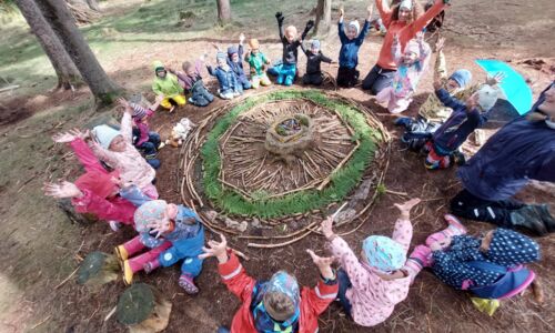 Kinder sitzen im Kreis im Wald, um etwas, dass sie aus Holz gebaut haben