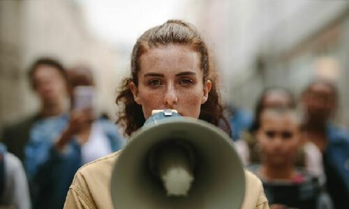 Eine junge Frau vor einer Menschengruppe hält ein Megafon vor das Gesicht